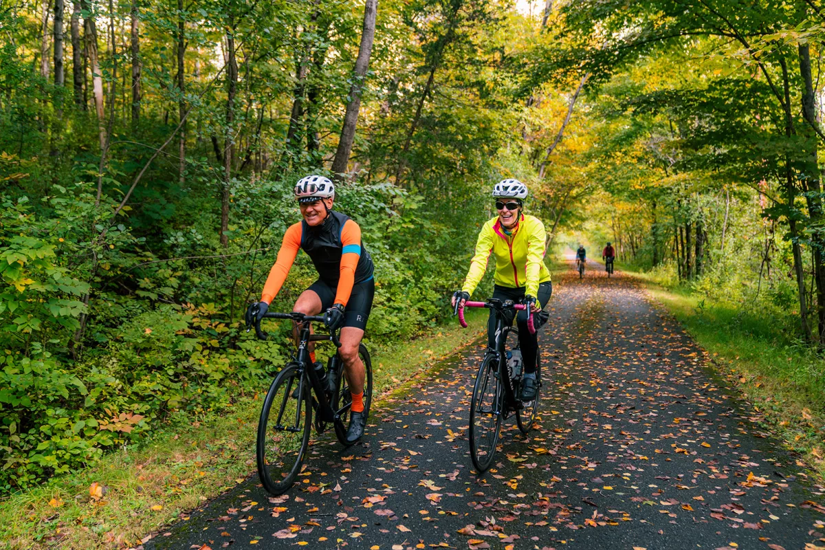 Two bikers biking down a tree lined road