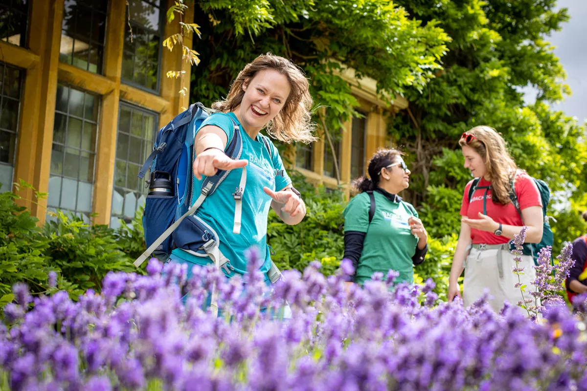 Woman smiling and pointing at the camera, with purple flowers surrounding her
