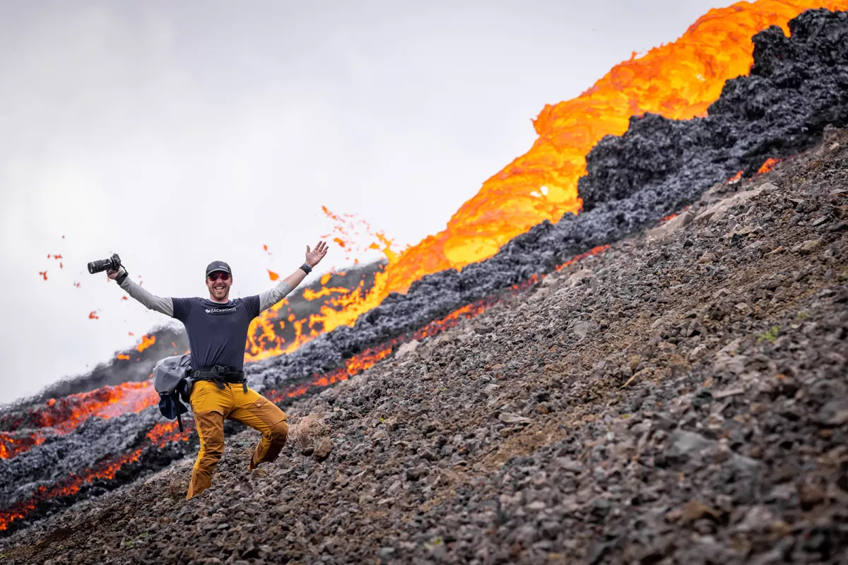 Man holding a camera with his arms wide open, in front of flowing magma