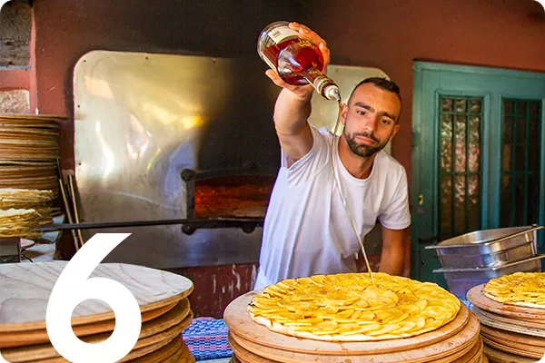 Number 6 overlayed a cook pouring oil over fresh pizzas 