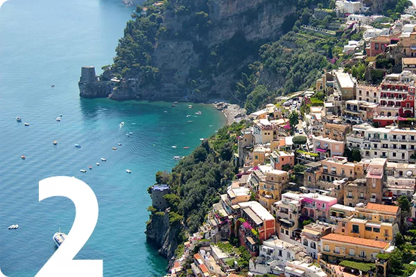 text:2; image: a seaside village built into a cliff overlooking blue water