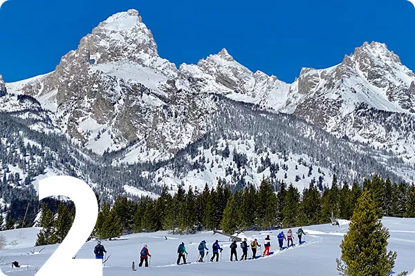 text:2; image: Hikers walking across a snowy field with a snowcapped mountain in the background