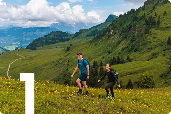 text:1; image: Two people hike up a grassy mountain range