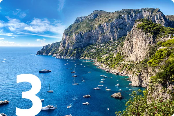 Rocky coastline next to blue water with boats in it