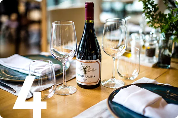 A table set with plates and wine glasses and a bottle of wine
