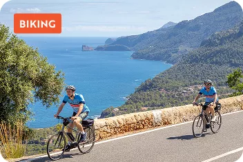 Two people biking on an empty road, with views of the ocean in the distance