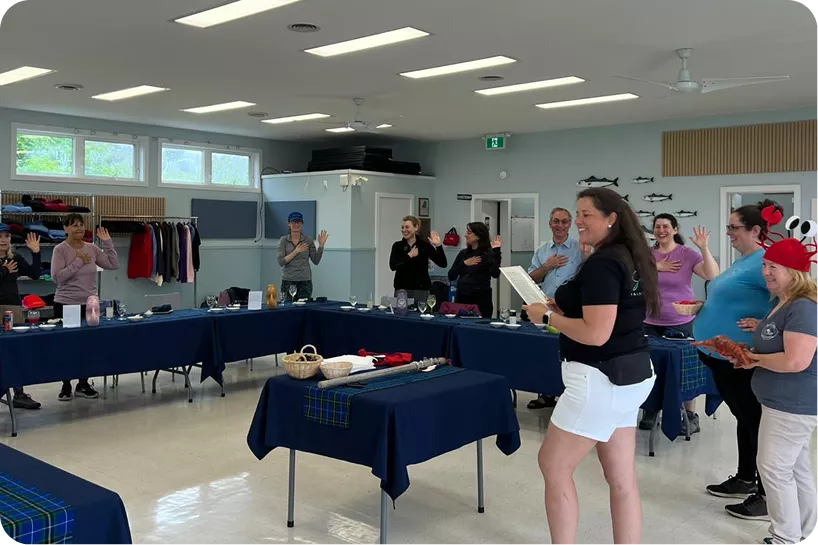 A group of people stand around a row of tables in a classroom