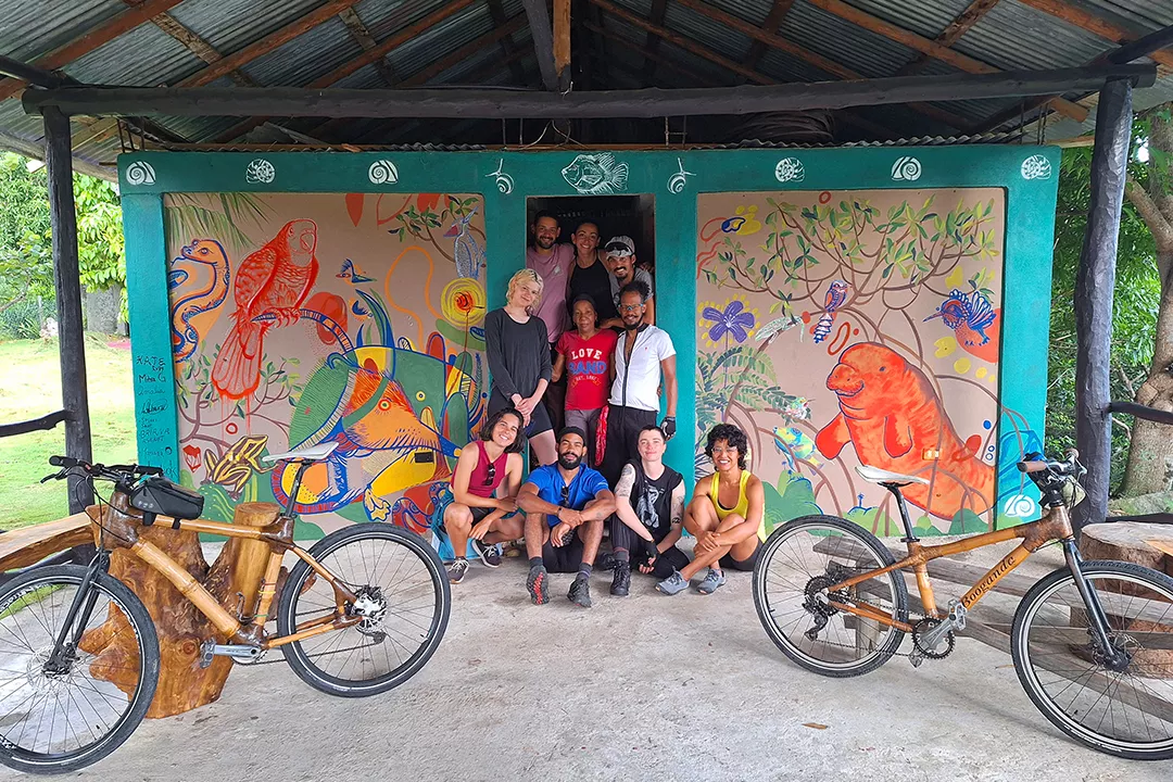Group of people smiling in front of an art mural with two bikes on either side