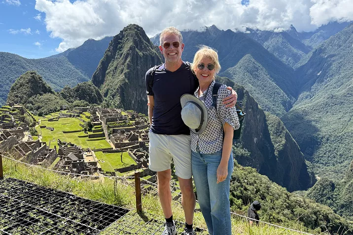 Man and woman hugging while standing on top of a grassy mountain