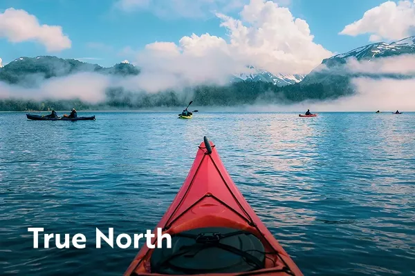 Tip of a red kayak looking over water with text overlay "into the wild"