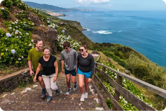Family of four walking up steep stairs on a mountain, with the ocean and a valley in the background