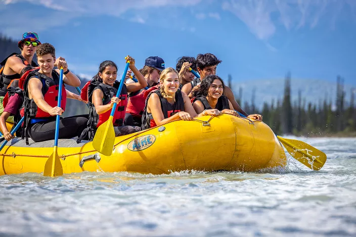 Group of people smiling while riding a yellow raft in a river
