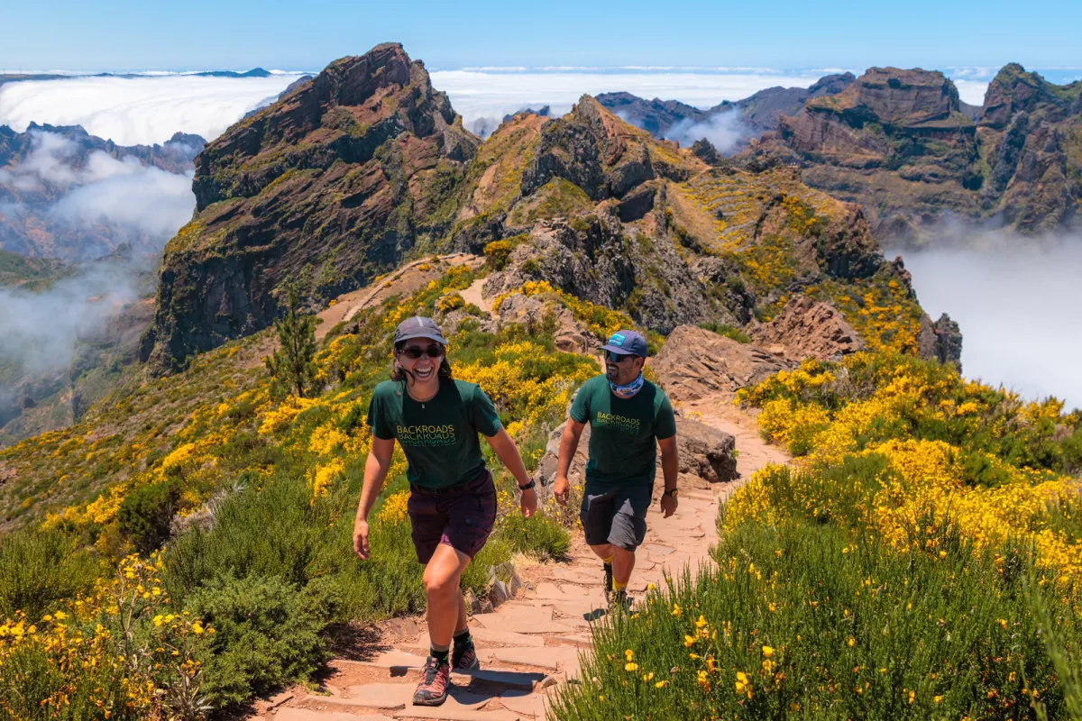 Man and woman ascending a mountain, surrounded by green and yellow plants