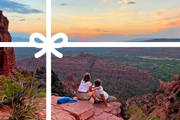 Two people sitting on a cliff looking out to a sunset