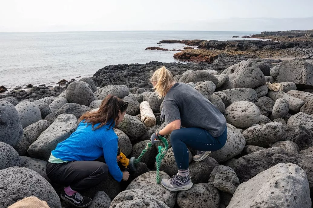 Two women kneeling on large rocks by the ocean