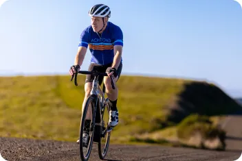 Man in a backroads jersey riding on his bike with a hilly landscape behind him.