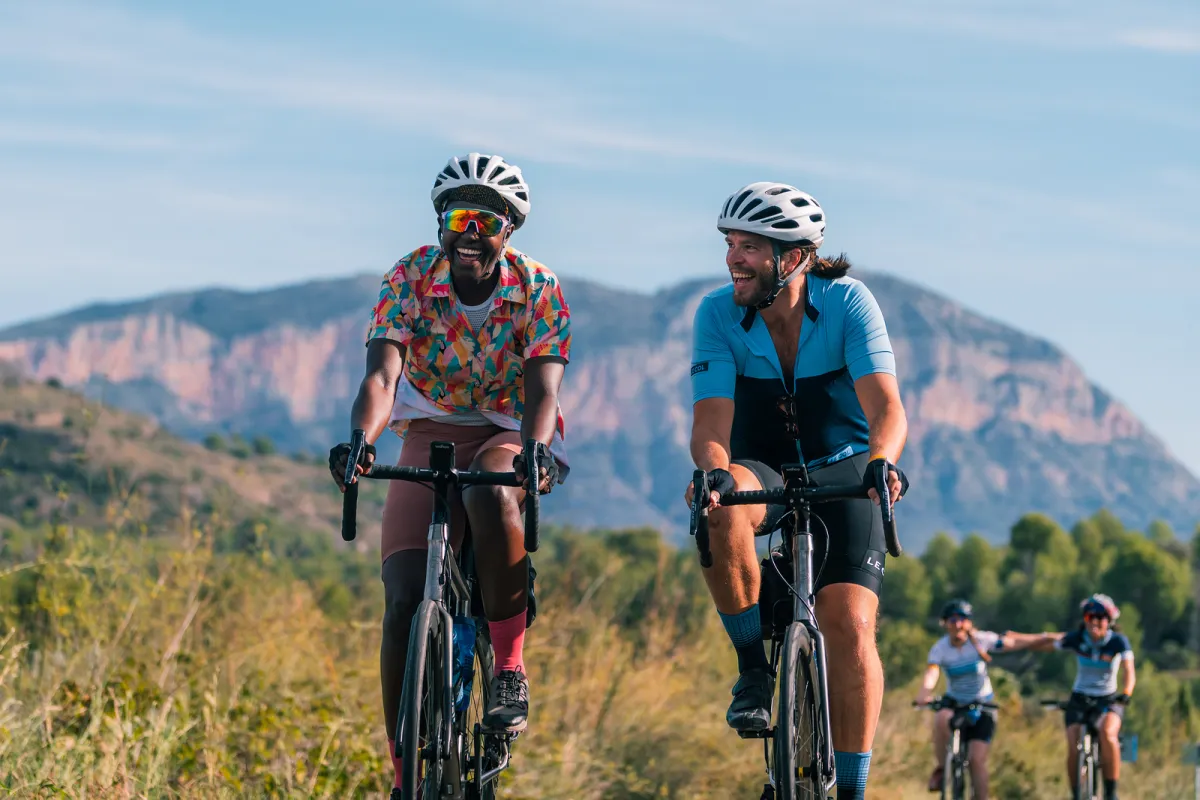 two men cycling next to each other with a mountain range in the background
