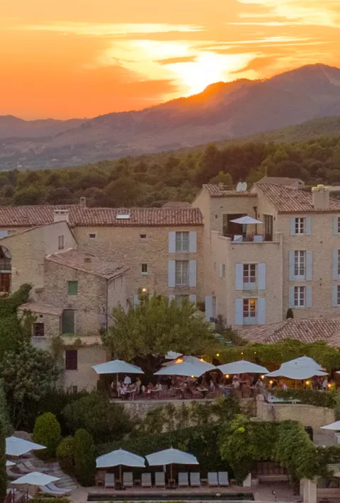 Tan buildings overlooked by mountains and the setting sun