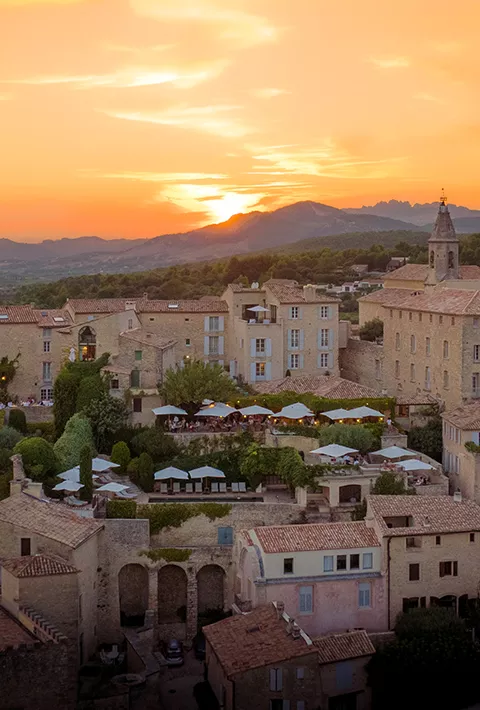 Tan buildings overlooked by mountains and the setting sun