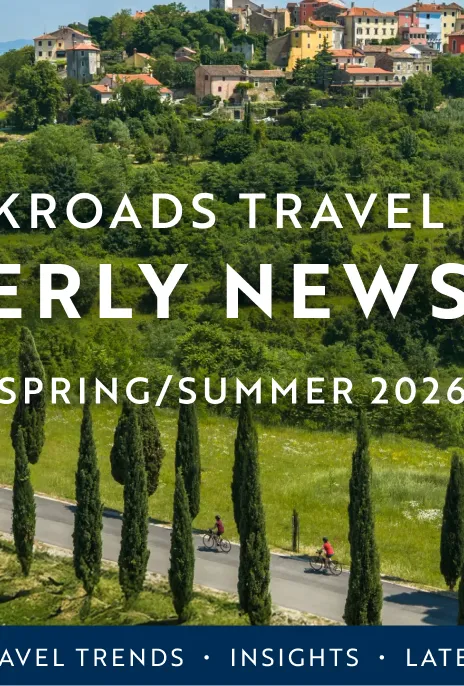 The Backroads Travel Advisor Quarterly Newsletter Spring/Summer 2026 is written over rolling hills with small multicolored homes and tree lined roads.