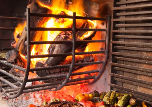 Food roasting next to fire, meat, zucchini, peppers, tomato etc.