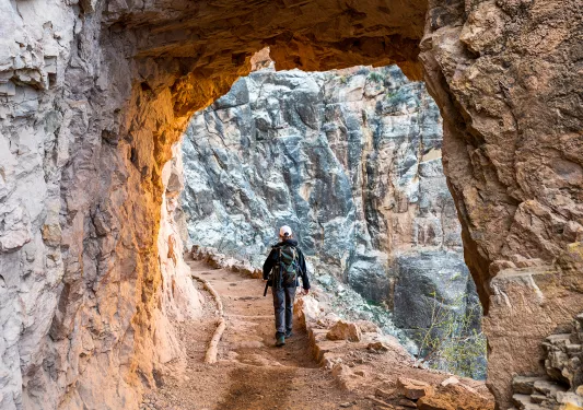 Archway shot of guest hiking down trail, towards rock face.