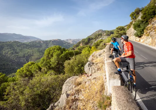 Bikers resting with bikes on side of a road in Spain, admiring a view.
