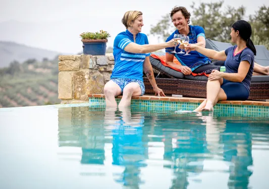 Three guests in biking gear dipping their feet in a pool.
