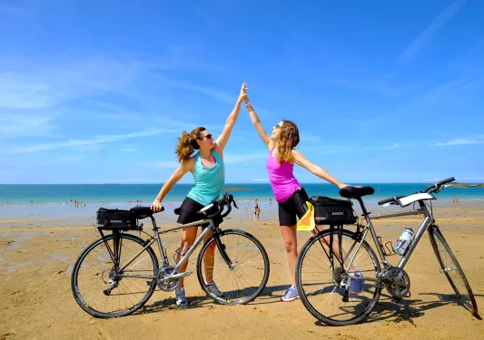 Two Backroads Guests High Fiving on Beach with Bicycles 