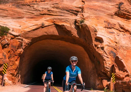Two bikers emerging out of rock tunnel