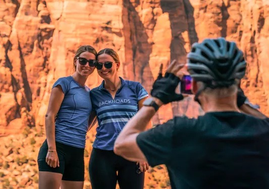 Guest taking photo of two others, all in bike gear, orange cliffs behind them.