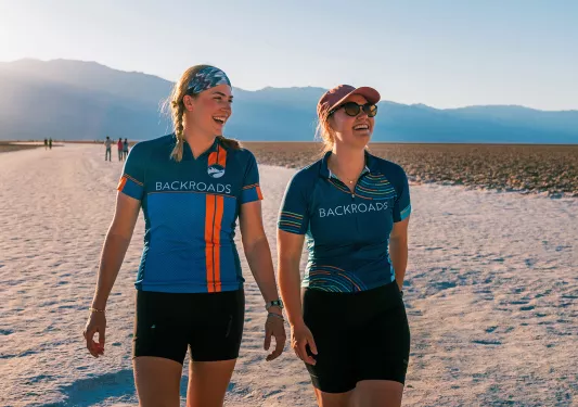 Two guests in BR jerseys walking along a sandy bank.