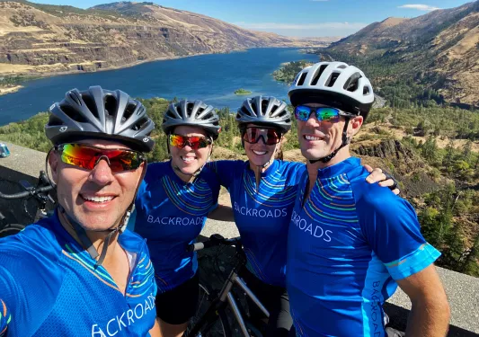 Four guests posing in front of large river/reservoir. 