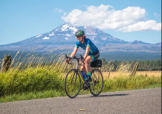 Guest cycling down grassy road, Mount Hood in background.