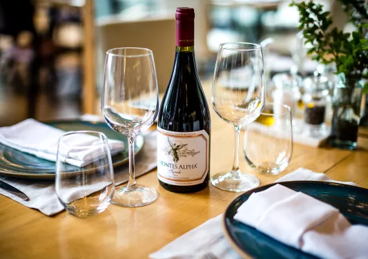 Shot of wine bottle, wine glasses, plates, etc. on table.
