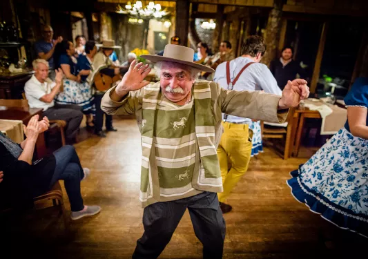 Local dancing in wooden hall, guests around them.