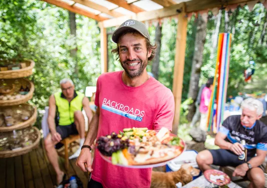 Leader presenting platter of food to camera, smiling.