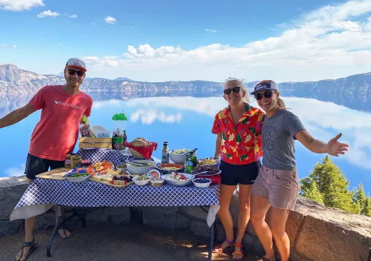Three guests next to lunch table, large lake in background.