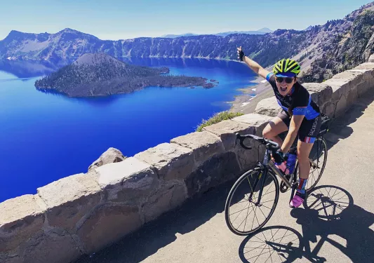 Guest cycling and gesturing towards Crater Lake on her right.