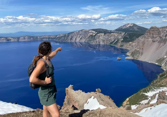 Guest on cliff's edge, pointing towards Crater Lake.