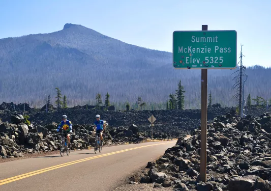 Two guests cycling past "MCKENZIE PASS" sign.