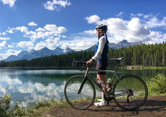 Guest standing next to bike, looking out to large lake, mountains beside them.
