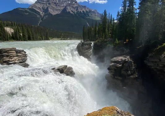 Point of view shot of large flowing waterfall, large mountains in background.