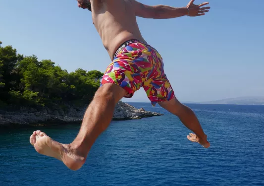 Shot of airborne guest jumping into water, others below.