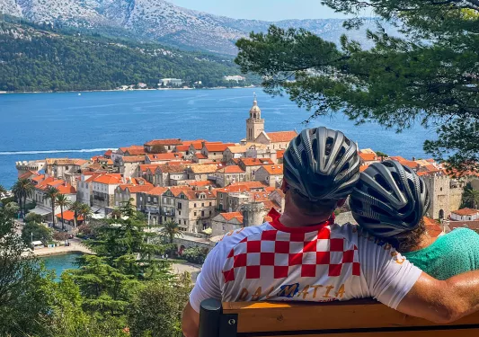 Two guests in bike gear on bench, overlooking Dalmatian Coast.