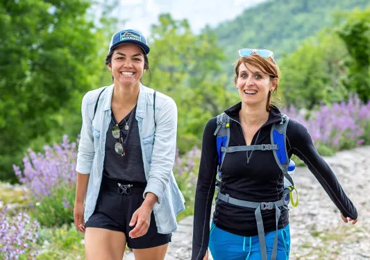 Two hikers on a trail with wildflowers.