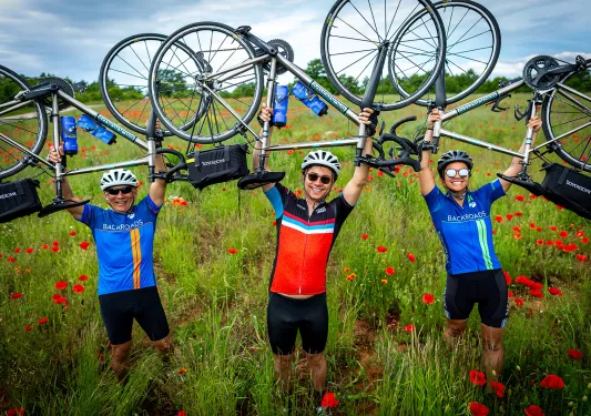 Three guests in flower field holding bikes over their heads.