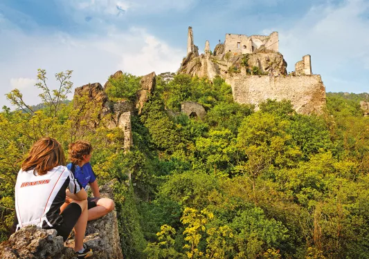 Two children sitting on a stone fence with building ruins in the background, Europe.