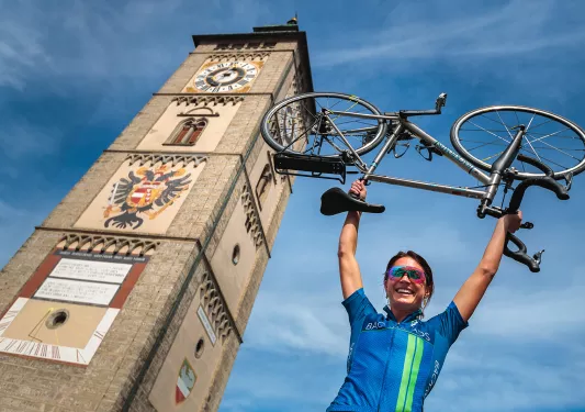 Biker holding a bike overhead with painted church tower in background. 