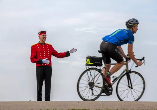 Biker riding past man in red uniform with gold buttons.